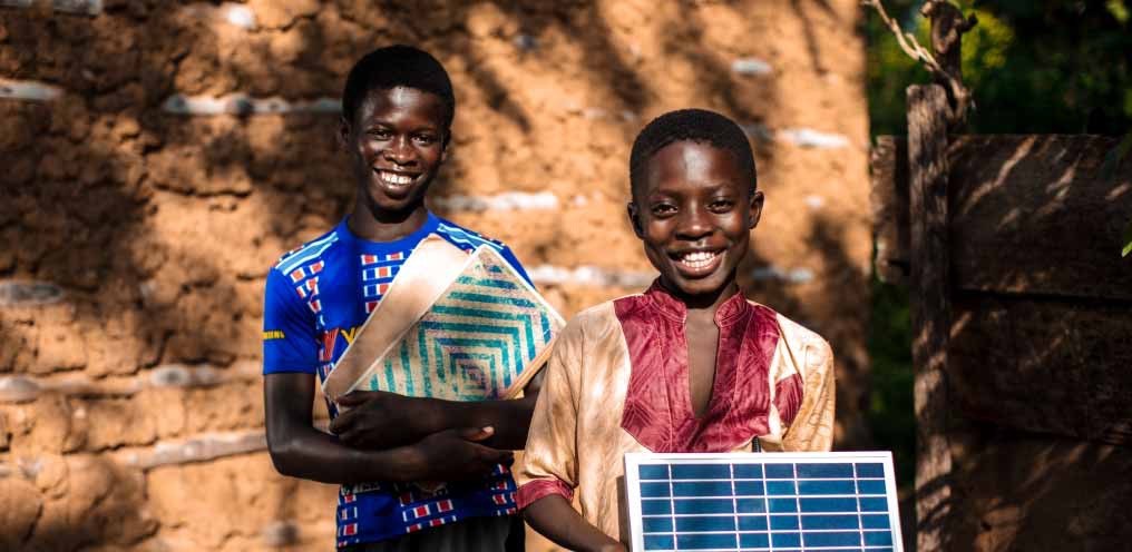 Two African children smiling while holding a solar panel